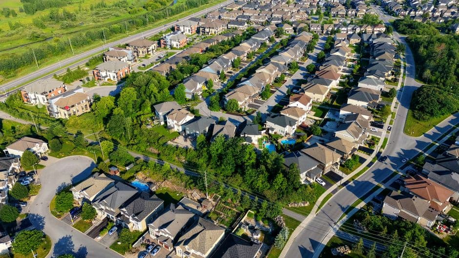 Aerial photograph of a suburban neighborhood showcasing uniform housing, lush trees, and surrounding roads.