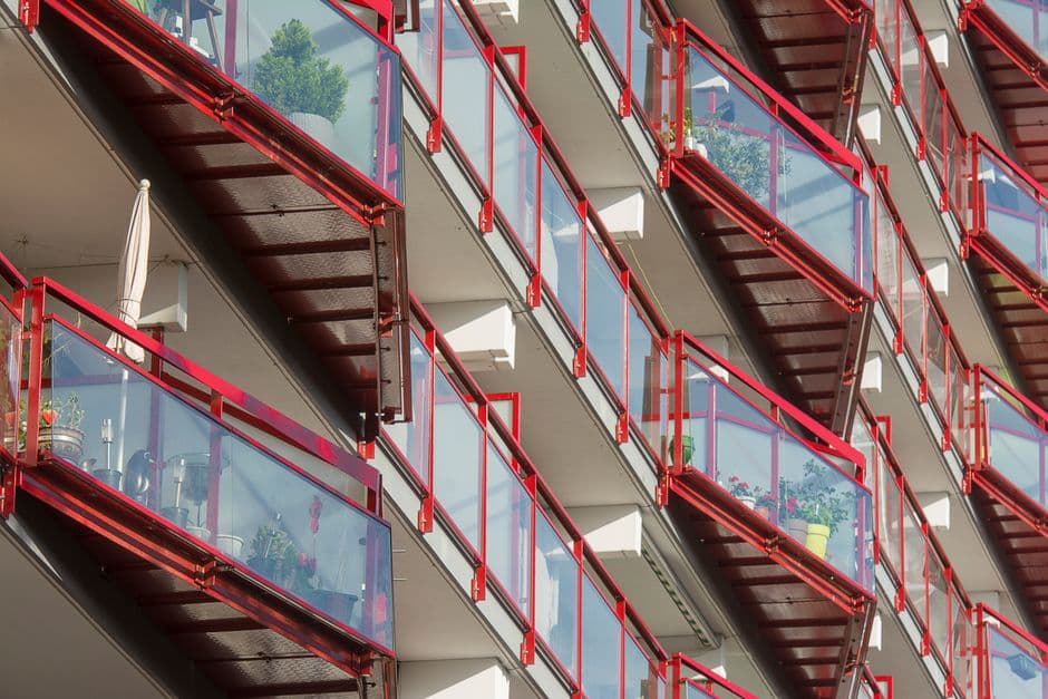 Dynamic view of modern urban apartment balconies featuring red railings and glass panels, showcasing contemporary architecture.