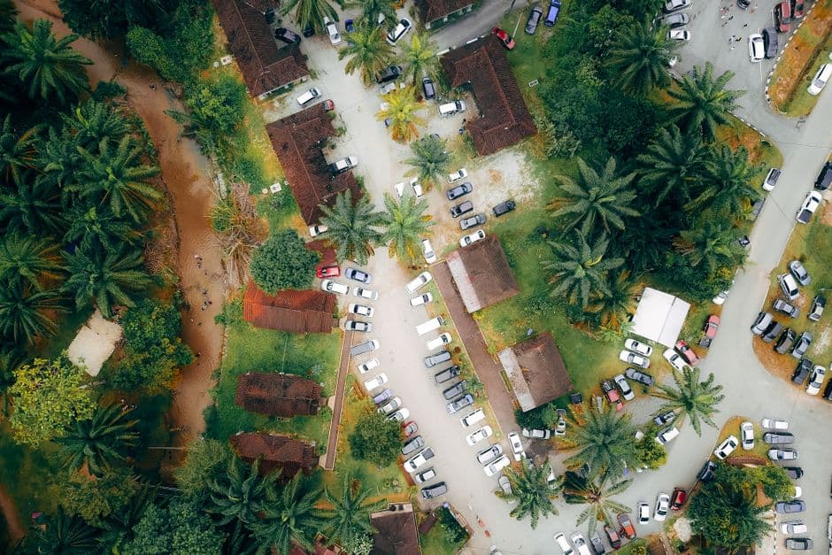 Drone view of automobiles parked near accommodation houses surrounded by green palms in tropical country