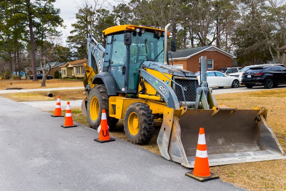 A large yellow construction vehicle with orange cones on a rural road near trees.
